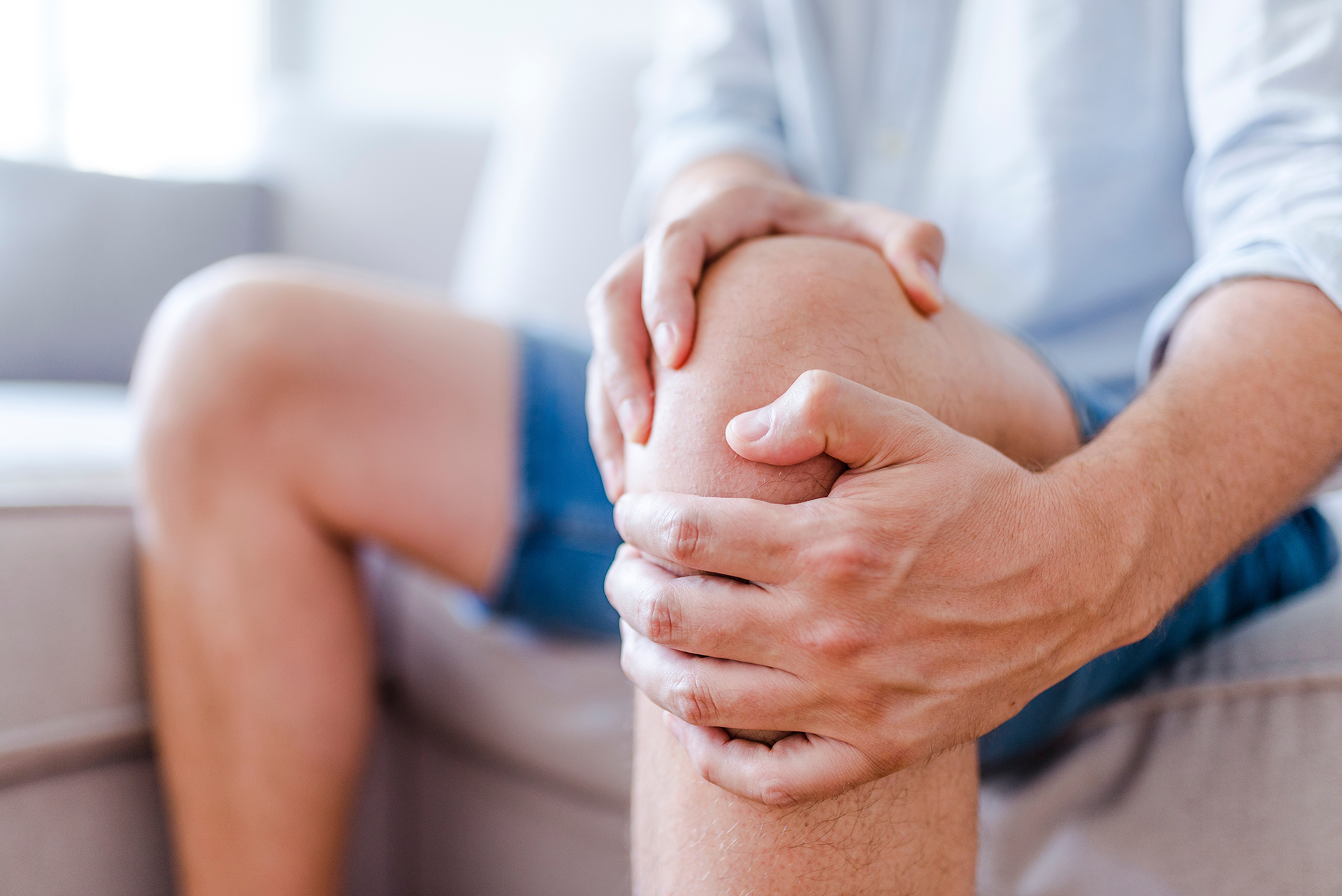 Man suffering from knee pain sitting sofa